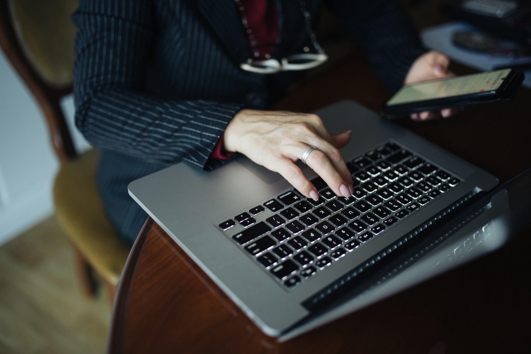 personne qui consulte un site sur son ordinateur portable en tenant un smartphone, dans un cadre professionnel