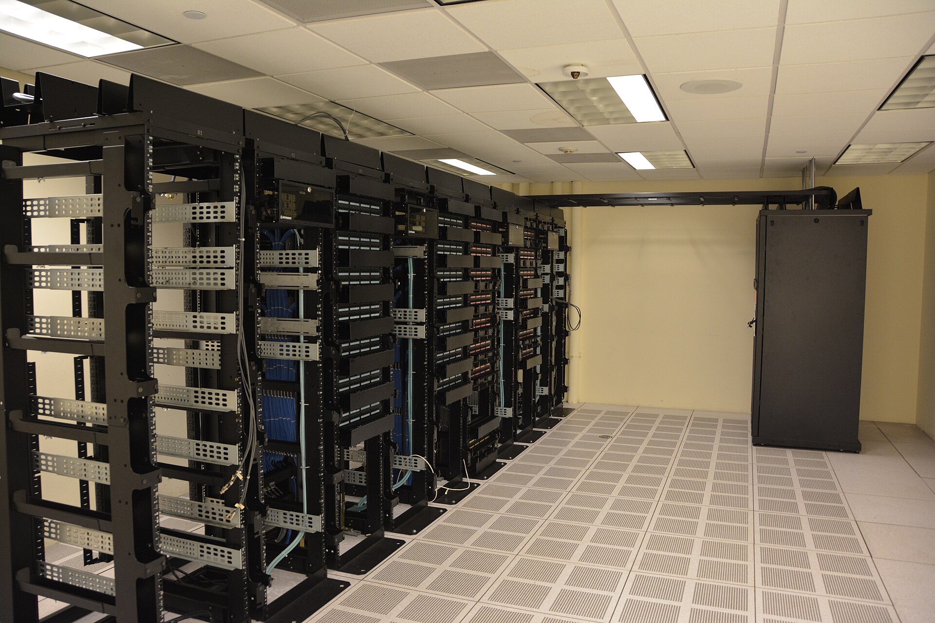 rangée de baies de serveurs informatiques noires dans une salle technique au faux plancher ventilé