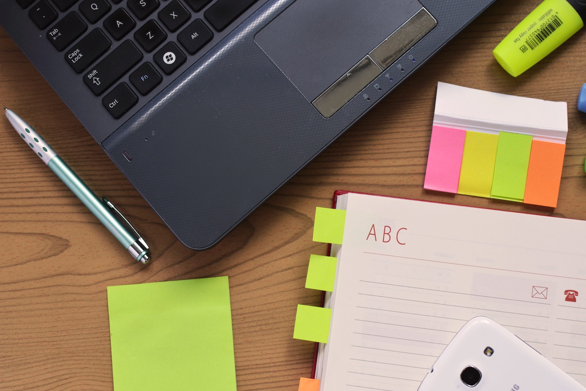 bureau vu de dessus avec un ordinateur portable, un carnet ouvert, des marque-pages adhésifs de couleur et un surligneur