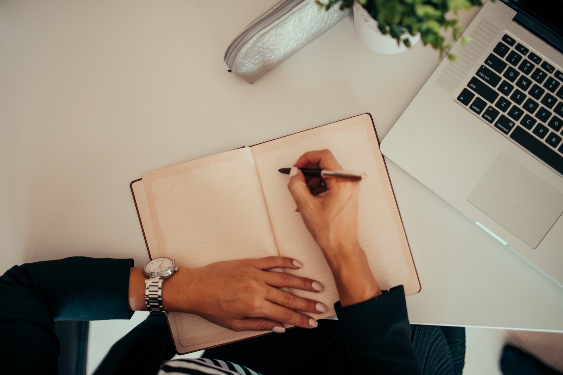 personne qui prend des notes à la main dans un carnet ouvert, à côté d'un ordinateur portable allumé